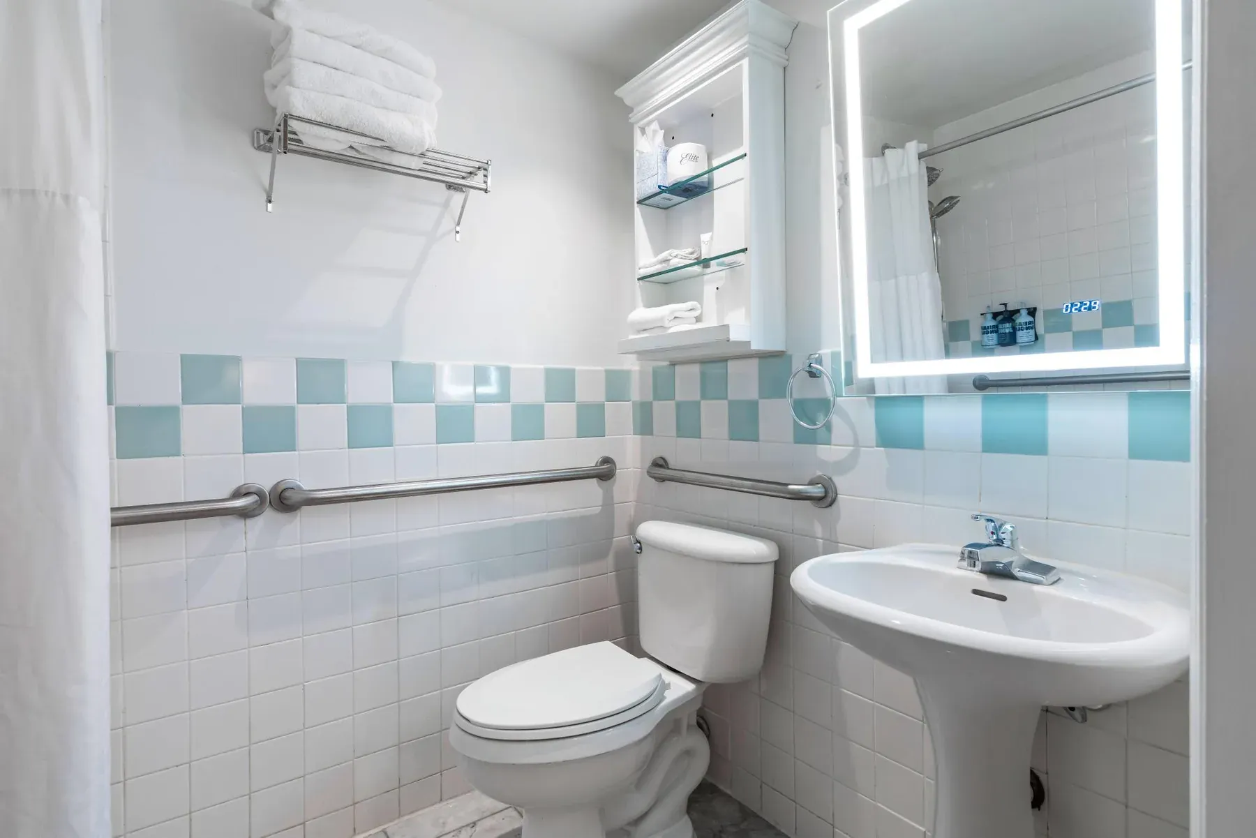 The bathroom basin and lit mirror, with grab bars either side of the toilet