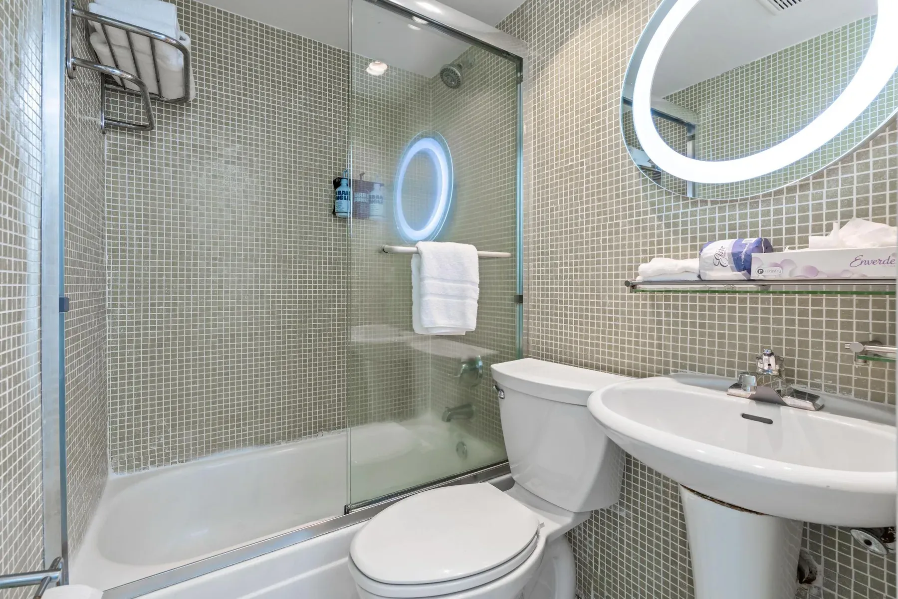 The bathroom, mosaic tile with a round lit mirror above the basin