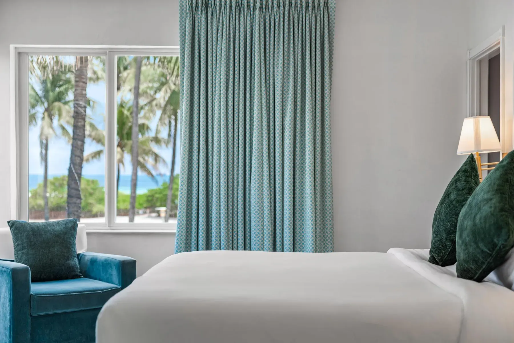 The king bed with the curtains drawn back to the palms and the water