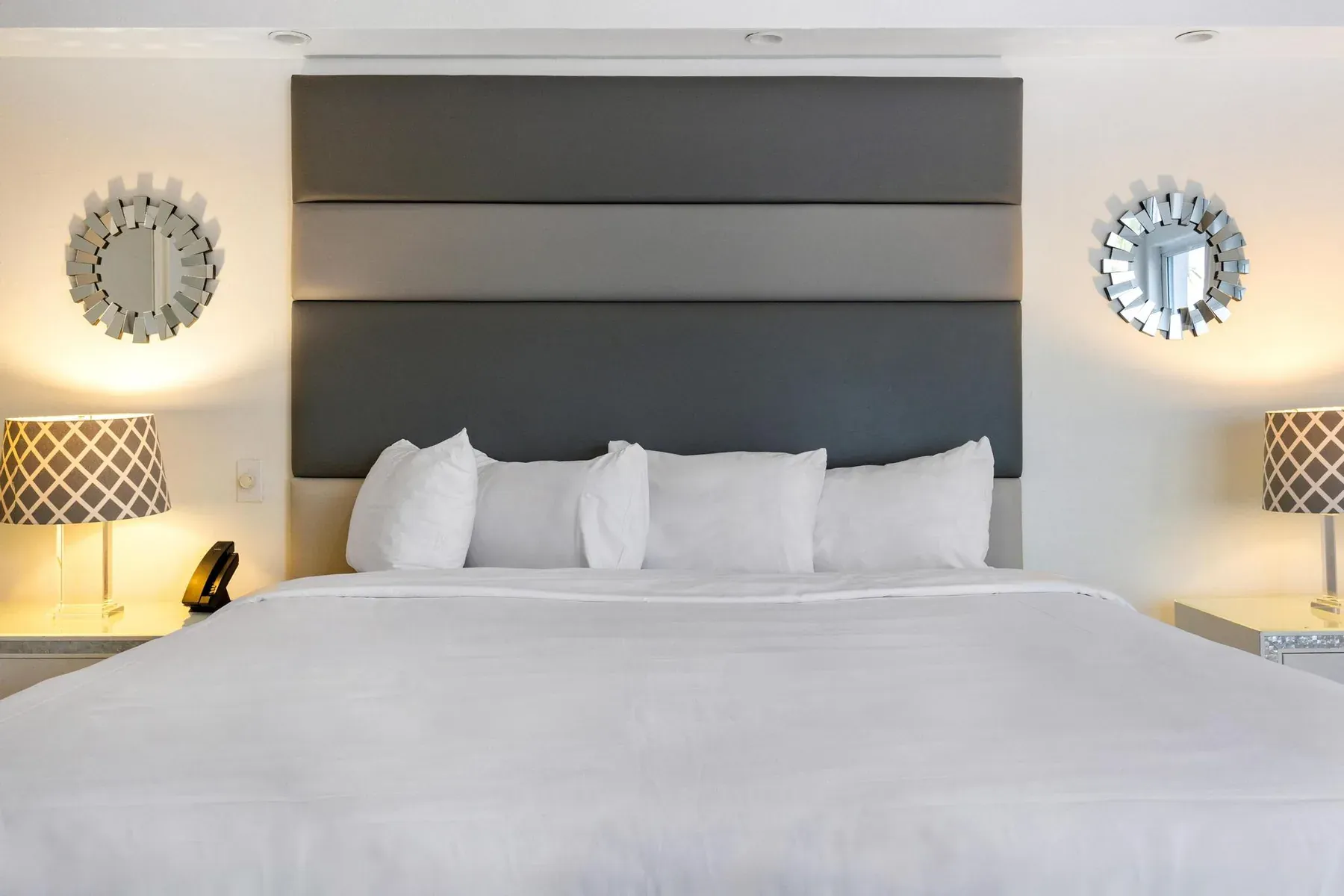 The king bed head-on, flanked by mirrored sunburst wall pieces and bedside lamps