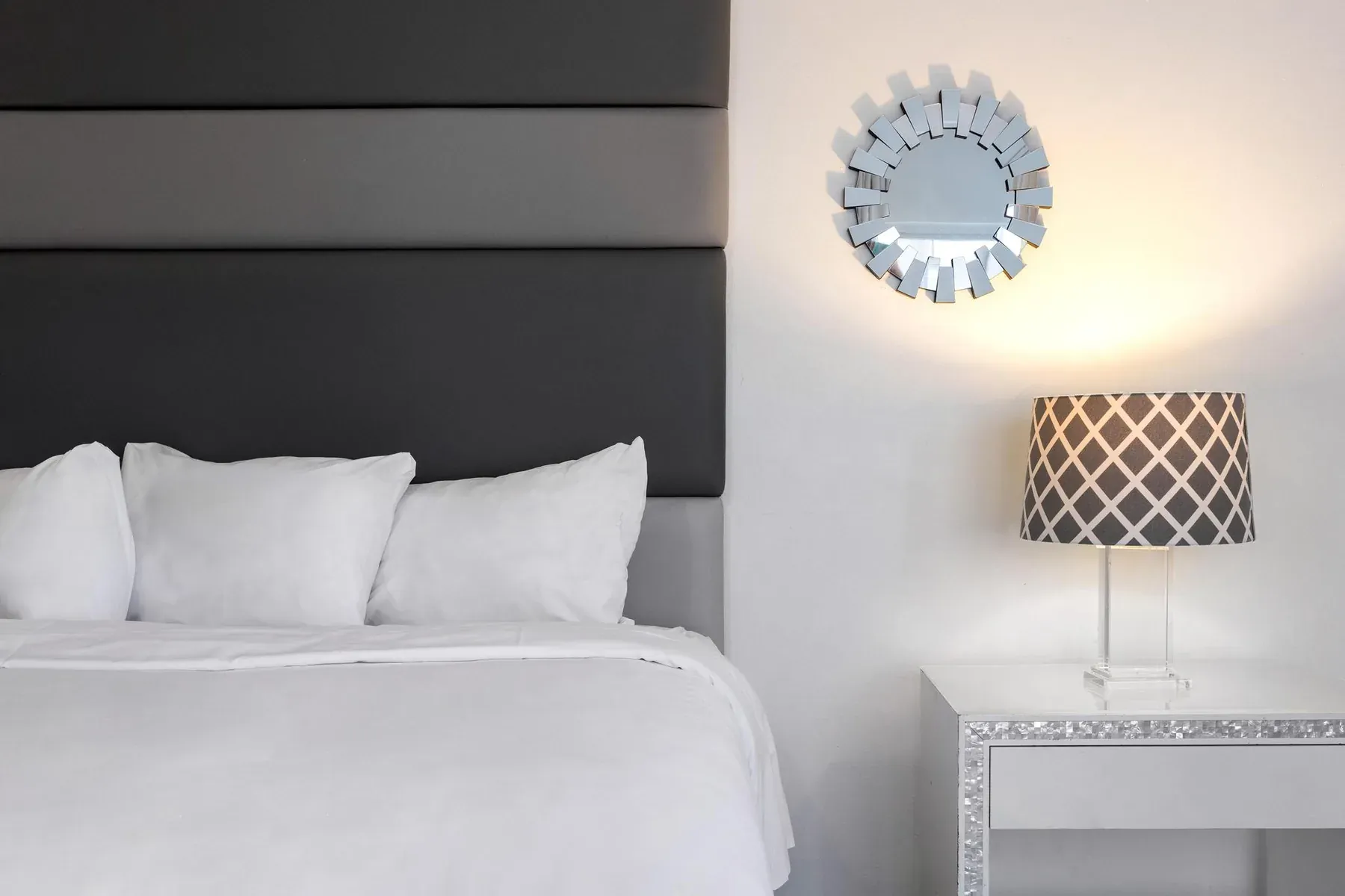 Bed detail, upholstered headboard and a sunburst mirror above the nightstand